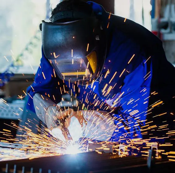 A welder wearing a protective mask, working intensely with sparks flying from the metal welding point.