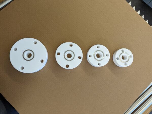 Four different sizes of white plastic parts on a brown surface.