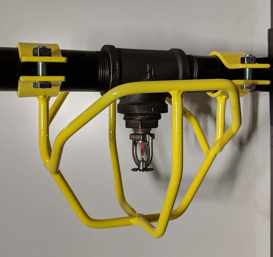 Yellow metal bracket mounted on a black pipe, securing a black and red electrical component.